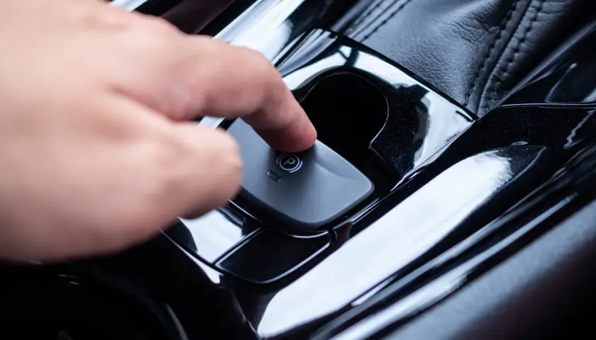 Main d'une personne appuyant sur le bouton du frein à main automatique. Voici comment débloquer un frein à main automatique.