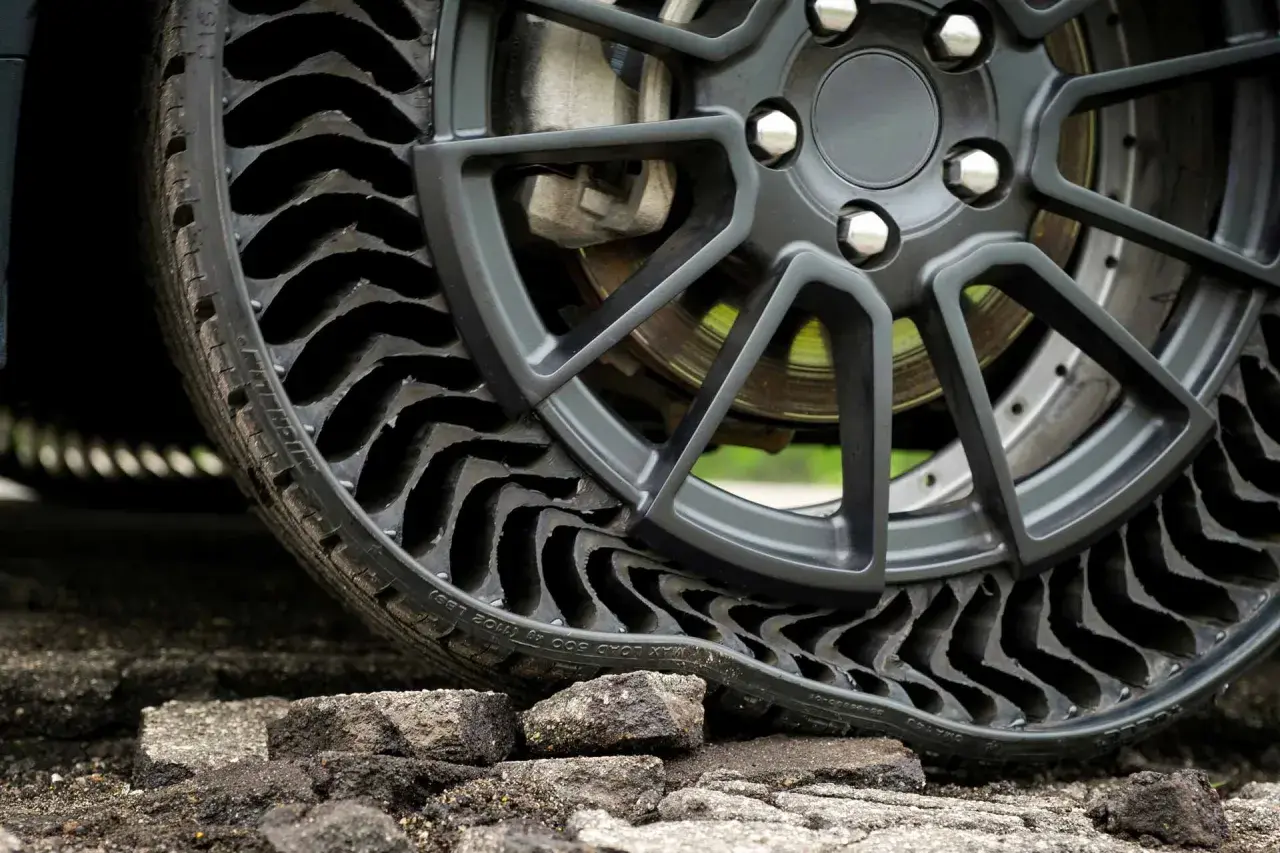 Gros plan sur une roue de voiture avec un pneu increvable, composé de multiples alvéoles noires, posé sur un sol dégradé.