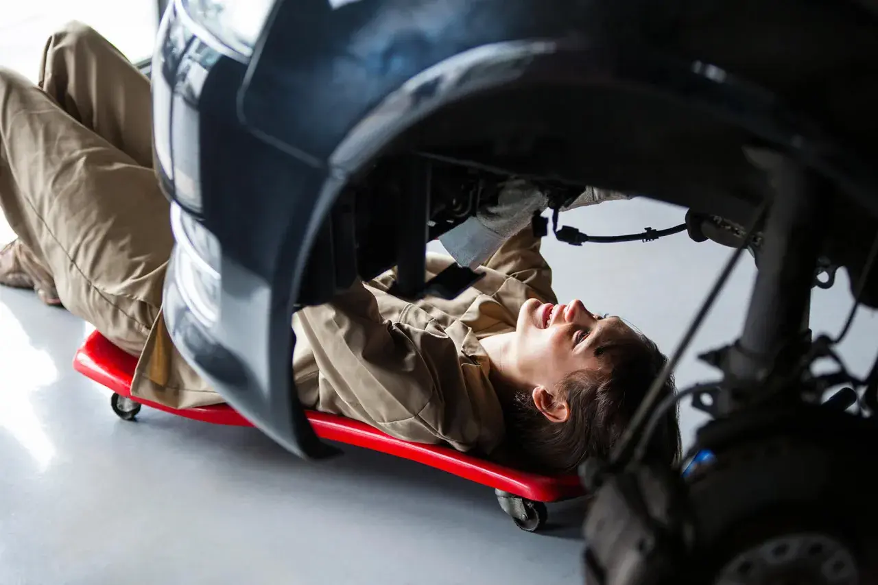 Mécanicienne travaillant sous une voiture, utilisant un chariot pour accéder à une pièce de réemploi.