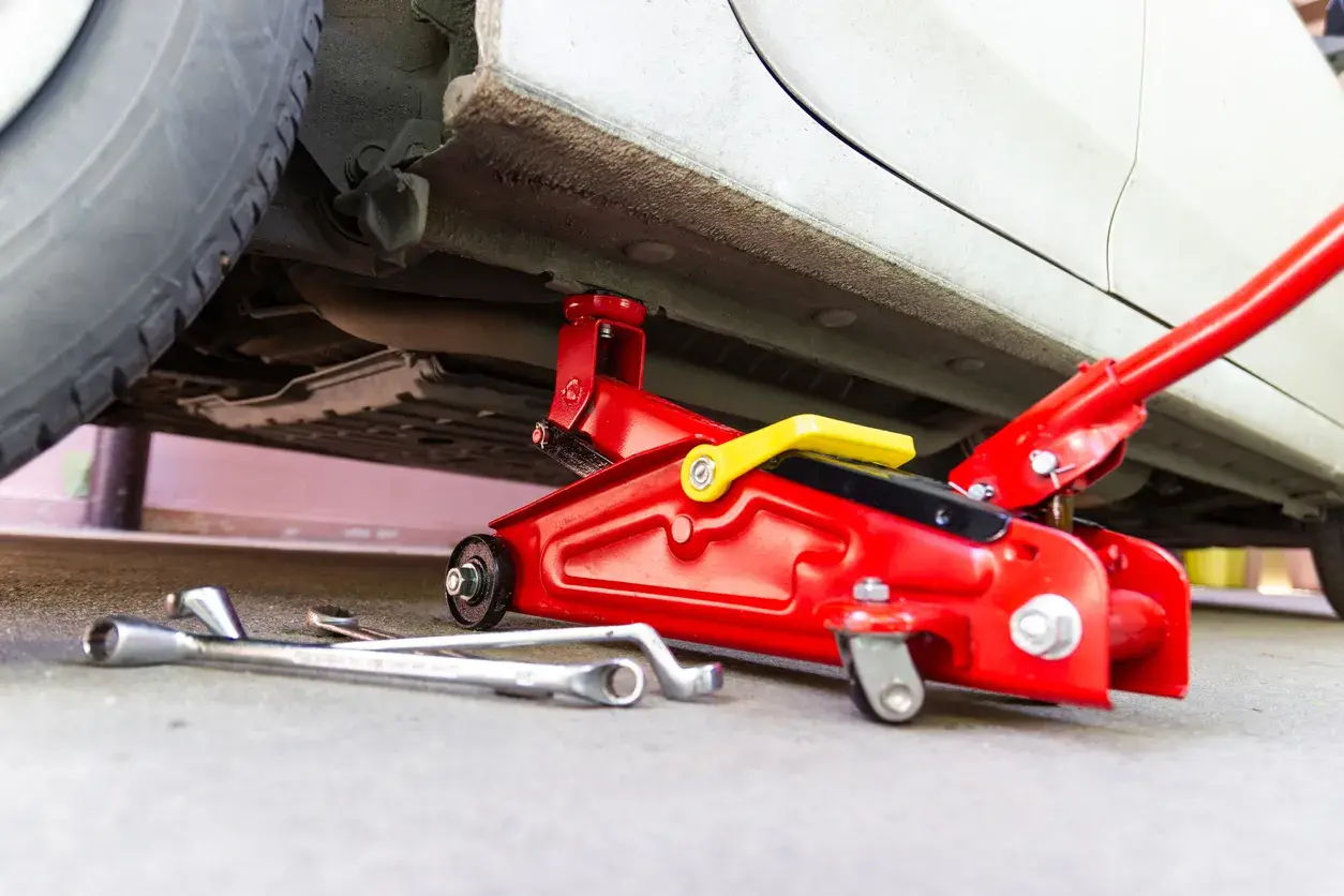 Un cric rouge est utilisé pour soulever une voiture. Des clés sont posées au sol, prêtes à être utilisées pour changer une roue.