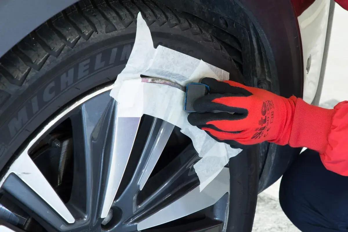 Main d'une personne portant un gant rouge et noir, utilisant un produit pour réparer jante alu.