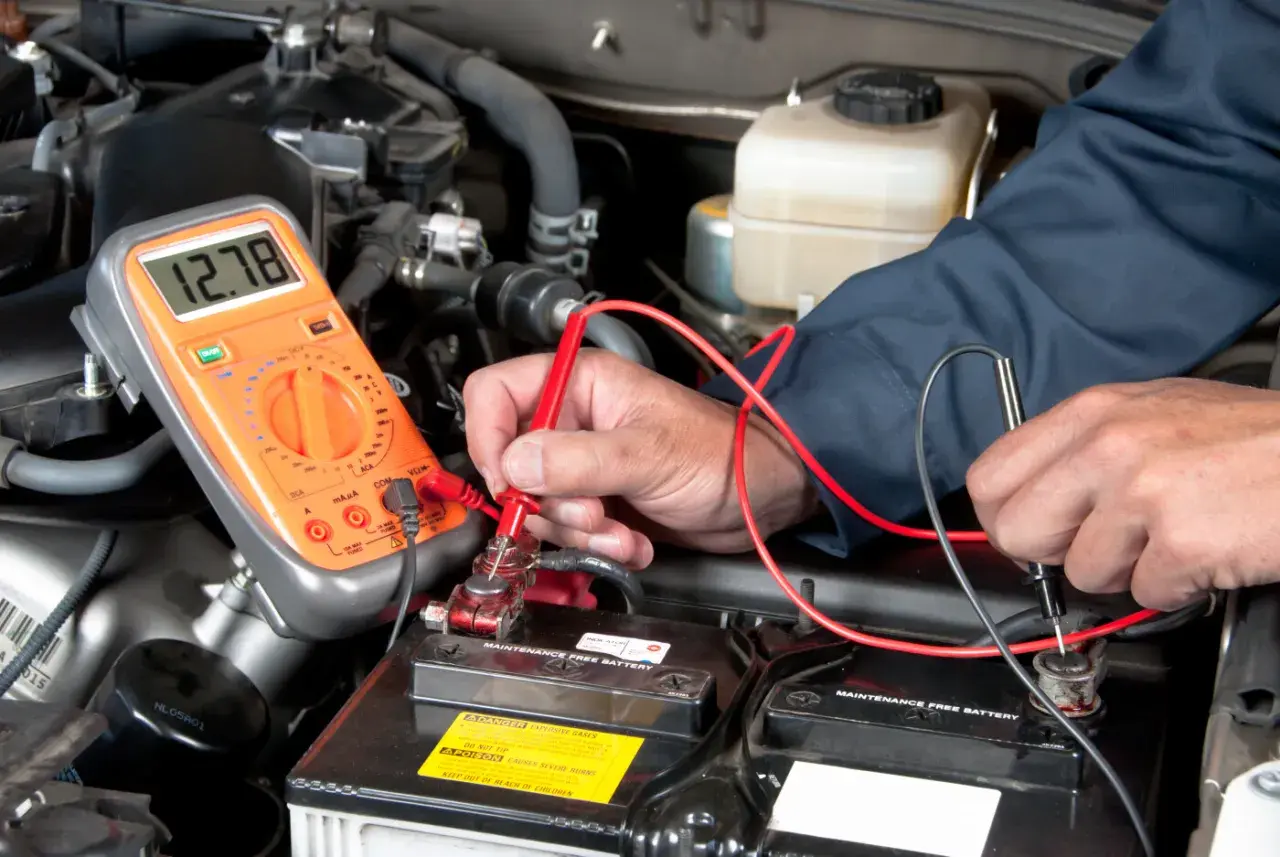 Un mécanicien vérifie la tension de la batterie d'une Mini Cooper. L'emplacement de la batterie est sous le capot, accessible pour le diagnostic.