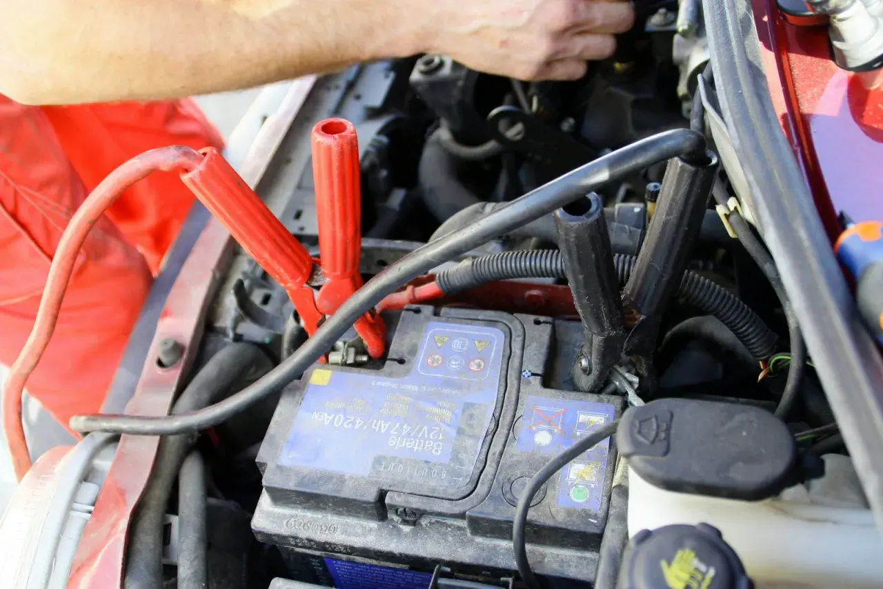 Comment brancher un booster de batterie : les pinces rouges et noires sont connectées à la batterie d'une voiture.