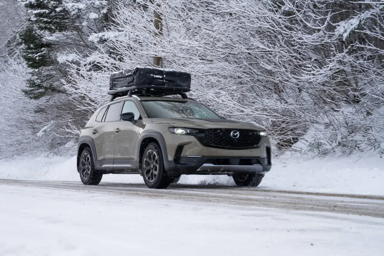 Un SUV gris roule sur une route enneigée, prêt à affronter l'hiver avec un coffre de toit chargé.