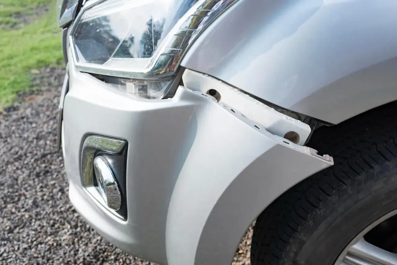 Le pare-chocs avant d'une voiture blanche est détaché, révélant une fissure carrosserie voiture. Le phare est visible.