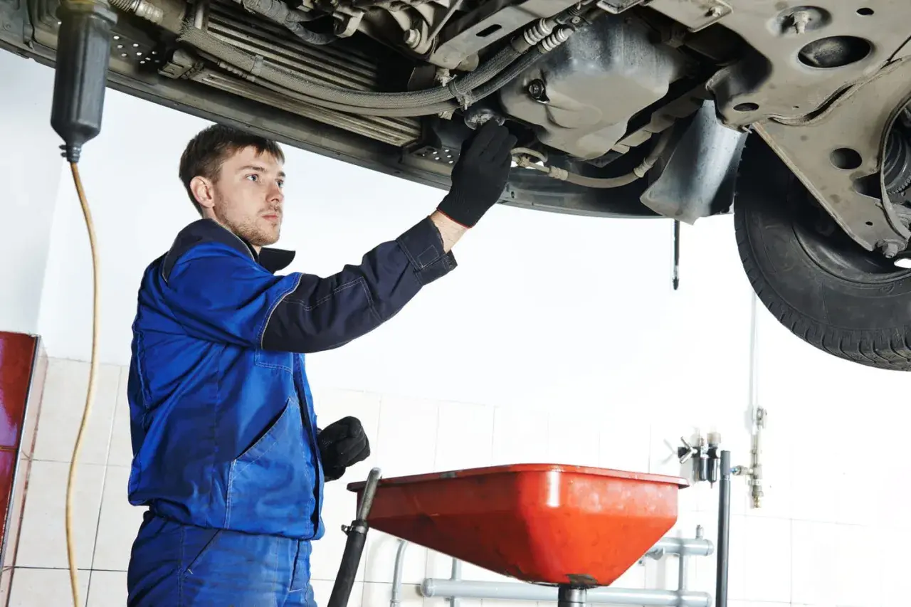 Mécanicien en bleu effectuant la vidange d'une voiture, prêt à changer l'huile. Savoir quand faire vidange voiture est essentiel.