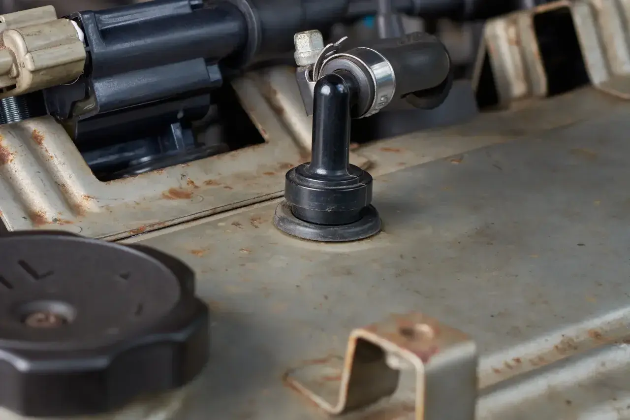 Détail d'un moteur de voiture, avec un tuyau noir fixé par un collier métallique. On aperçoit une pièce en caoutchouc noir, peut-être pour supprimer le reniflard d'huile.