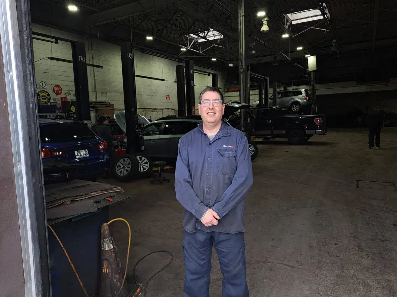 Homme souriant dans un garage libre service pour réparer soi-même. Plusieurs voitures sur des ponts élévateurs.