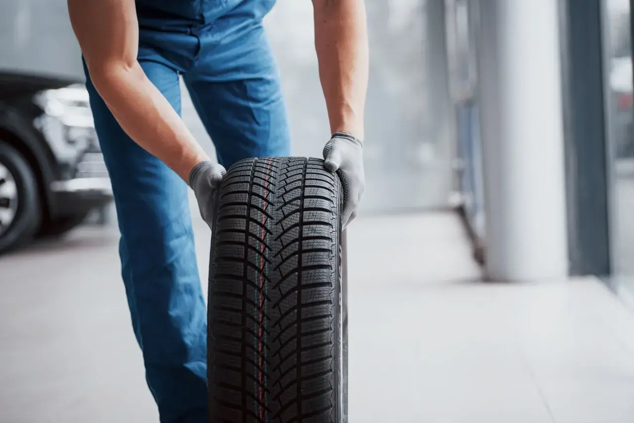 Un mécanicien en bleu tient un pneu d'hiver, une sous-marque Michelin, prêt pour le montage.