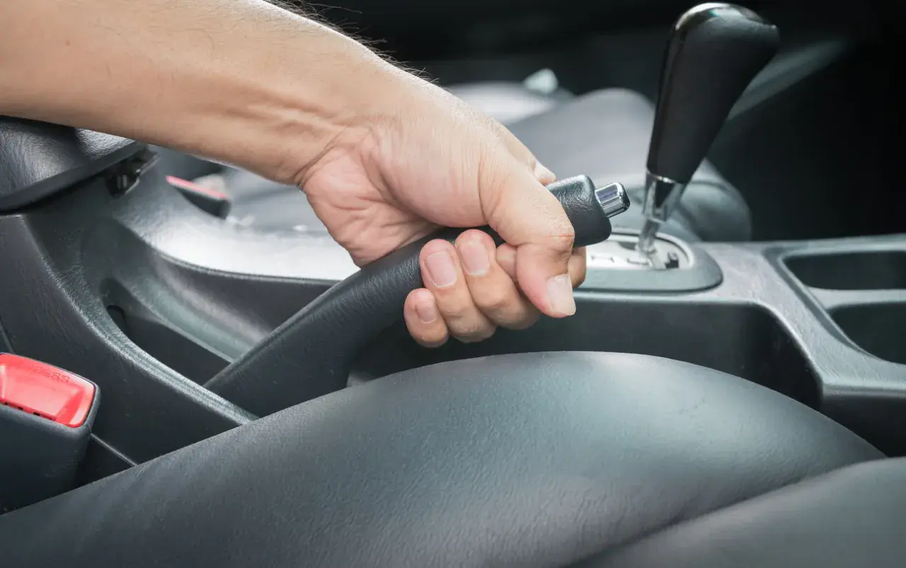 Main d'un conducteur actionnant le frein à main bloqué dans une voiture.