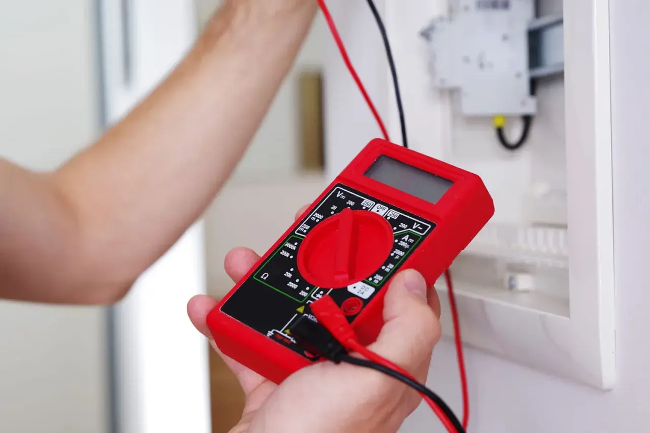 Main rouge pour tester un fusible voiture avec un multimètre.