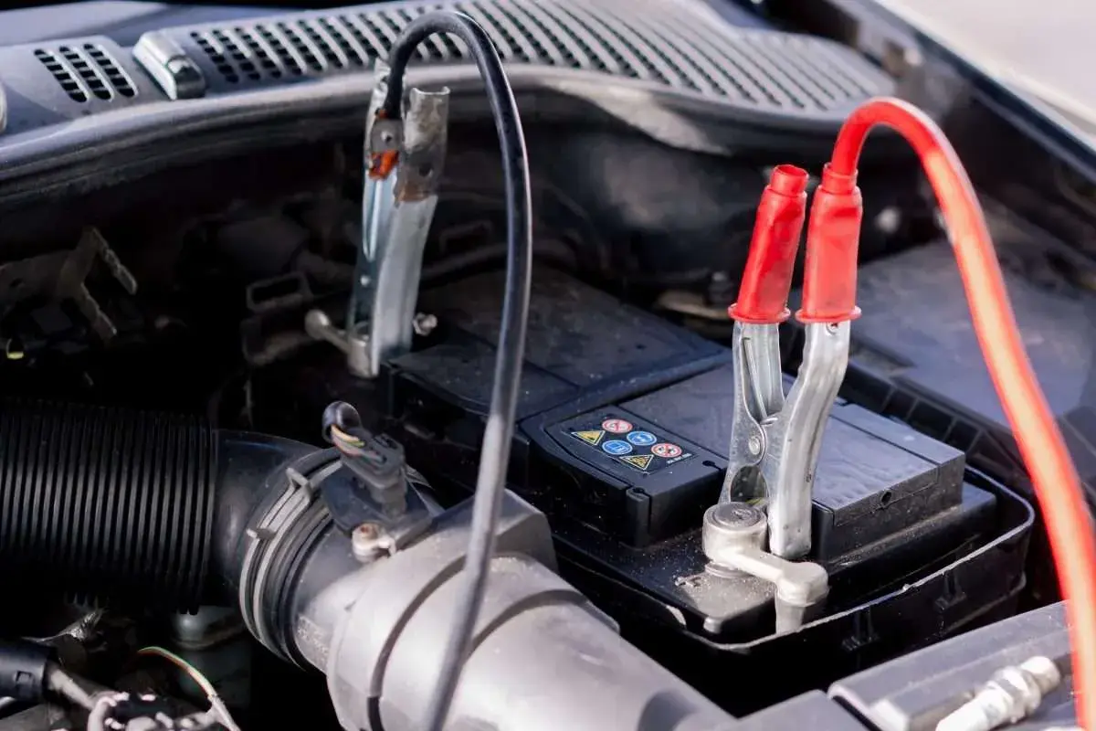 Pinces de démarrage connectées à une batterie de voiture, signe d'une conséquence batterie faible voiture.
