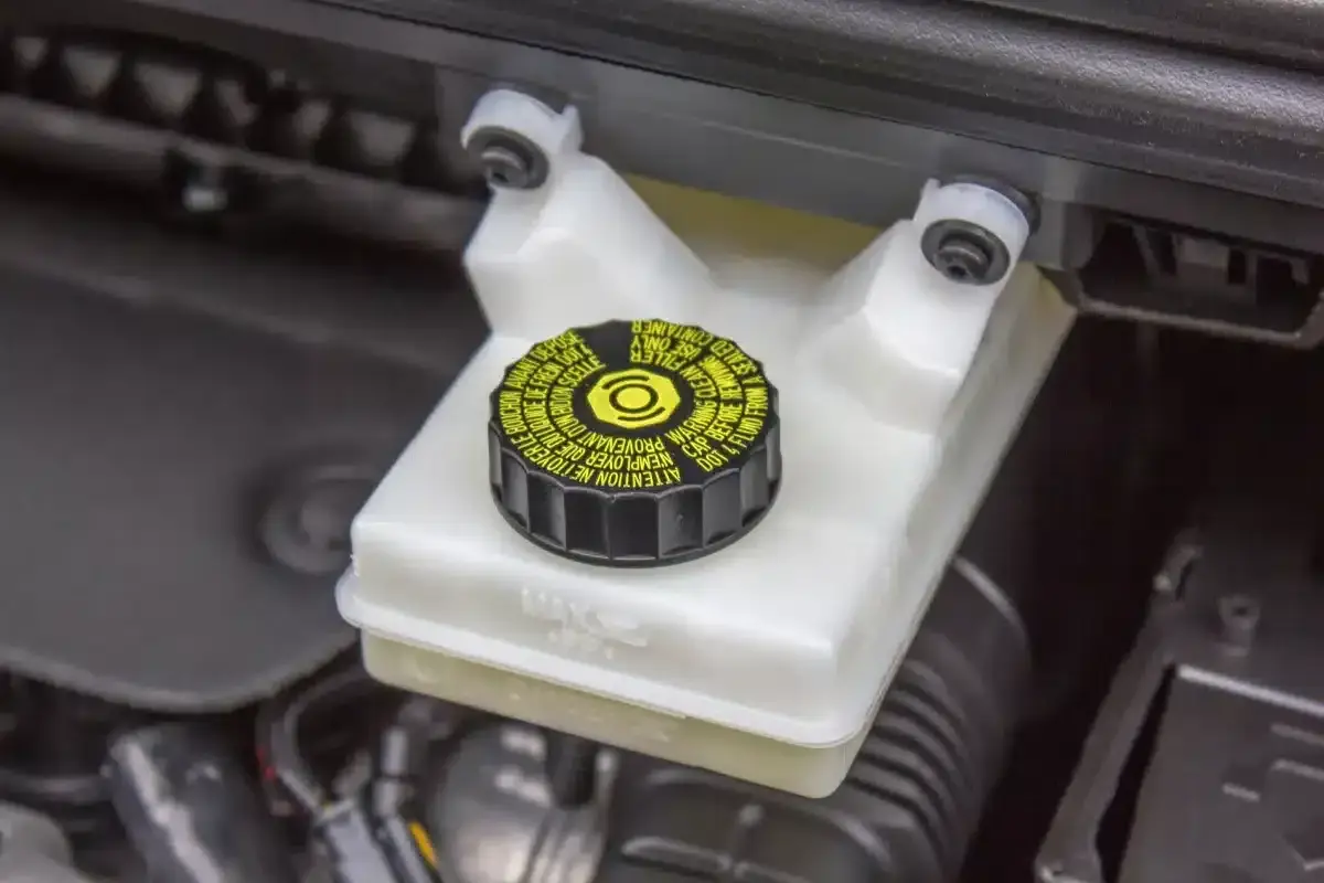 Réservoir de liquide de frein avec bouchon noir et jaune. Le niveau du liquide est visible, indiquant la nécessité d'un contrôle du liquide de frein.