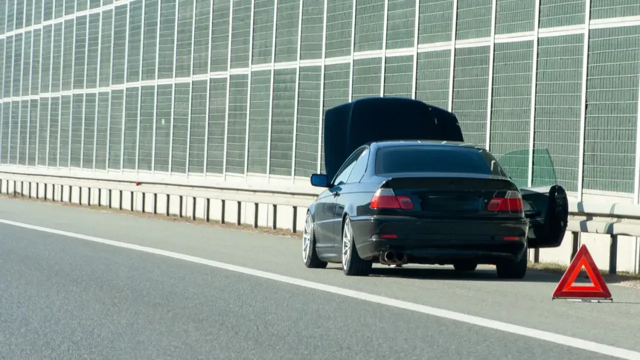 Panne sur l'autoroute. Capot ouvert, portière conducteur ouverte, triangle de signalisation rouge. Un entretien véhicule s'impose.