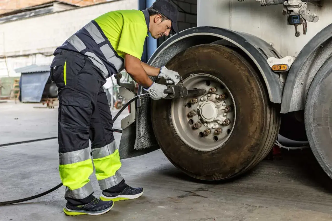 Un mécanicien en tenue de travail effectue le couple serrage roue voiture d'un camion avec une clé à chocs.