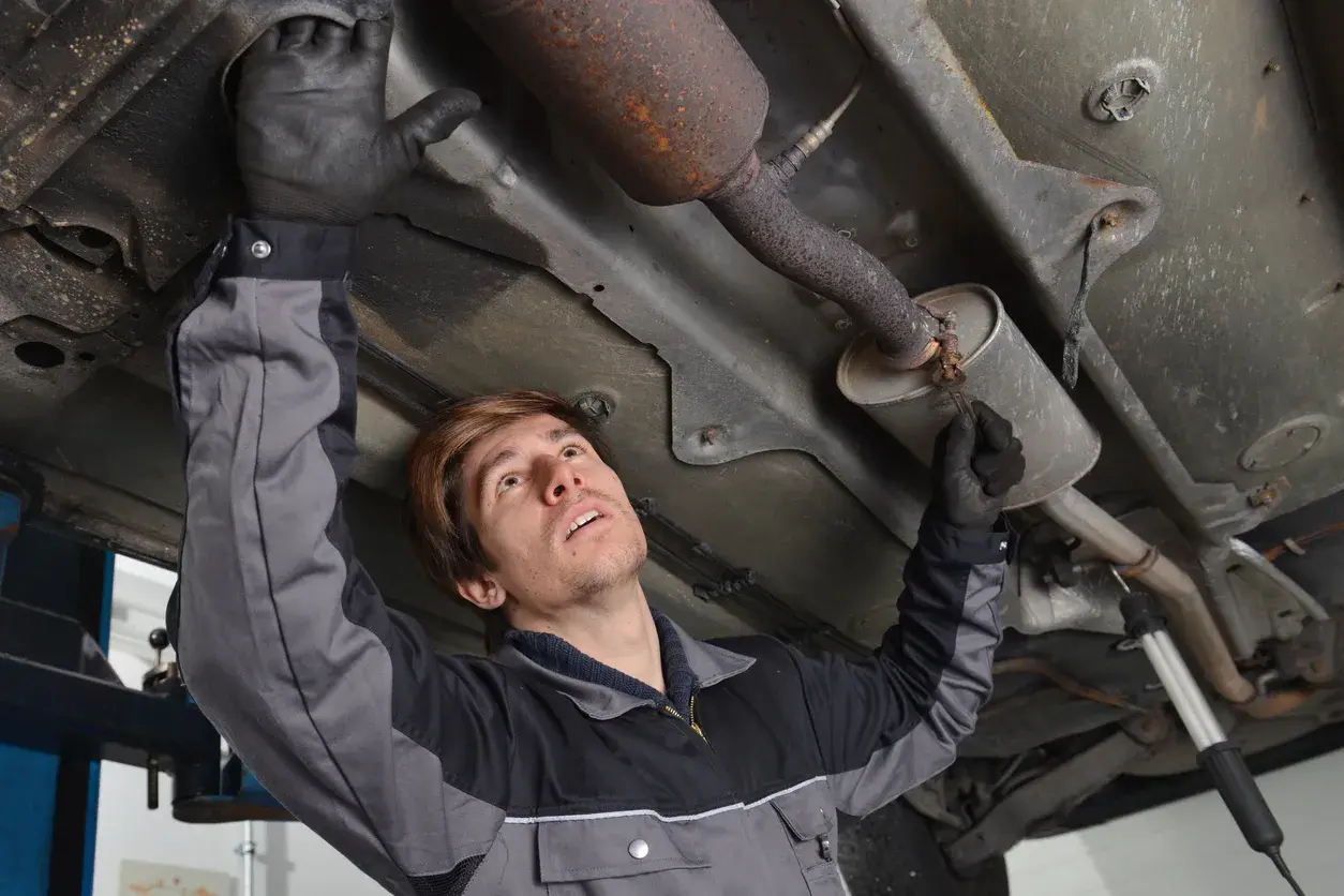 Mécanicien inspectant le pot catalytique d'une voiture, sous le véhicule.