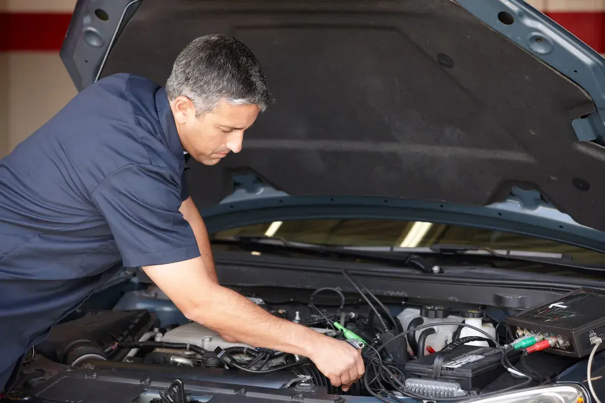 Mécanicien diagnostiquant un problème de démarrage à chaud sur un moteur de voiture avec un appareil électronique.