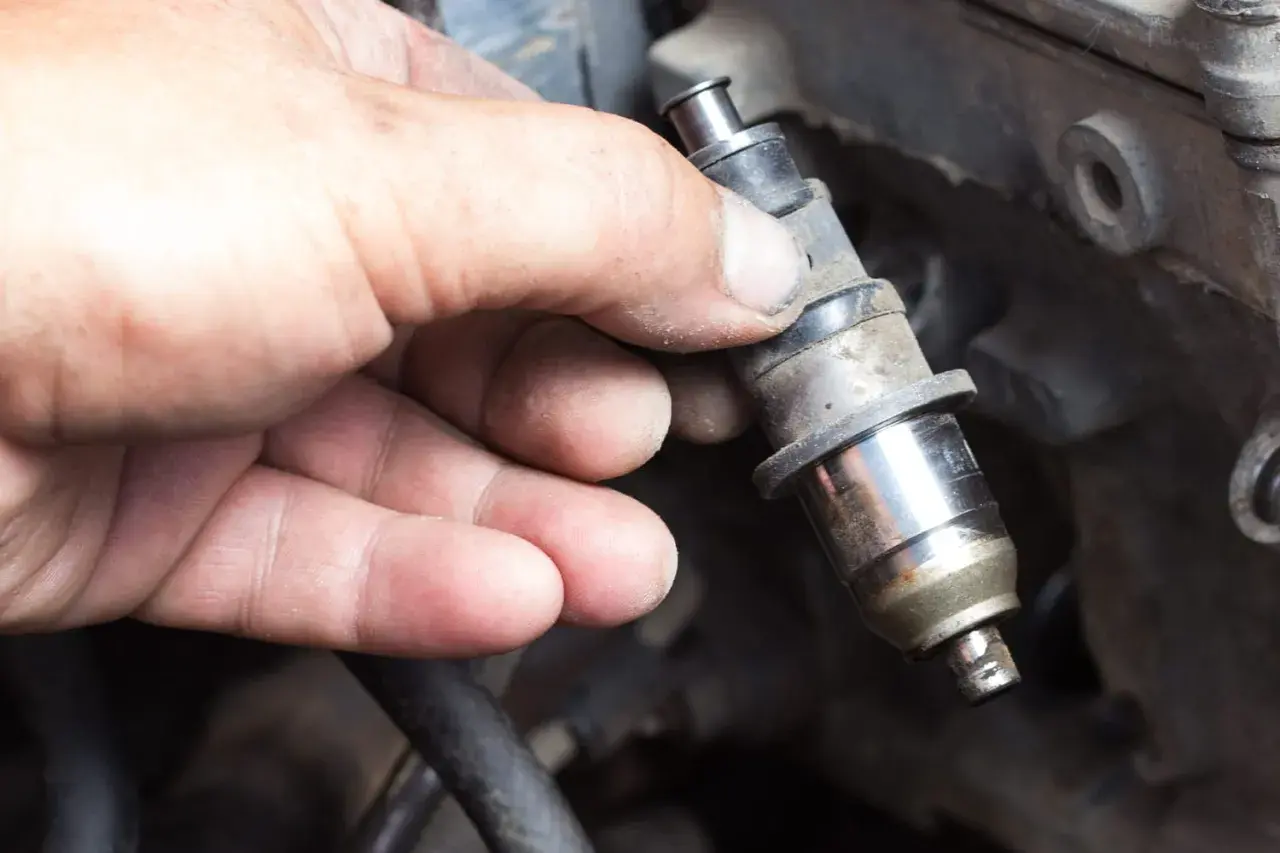 Main d'un mécanicien tenant un injecteur diesel sale, prêt à nettoyer injecteur diesel soi-même.