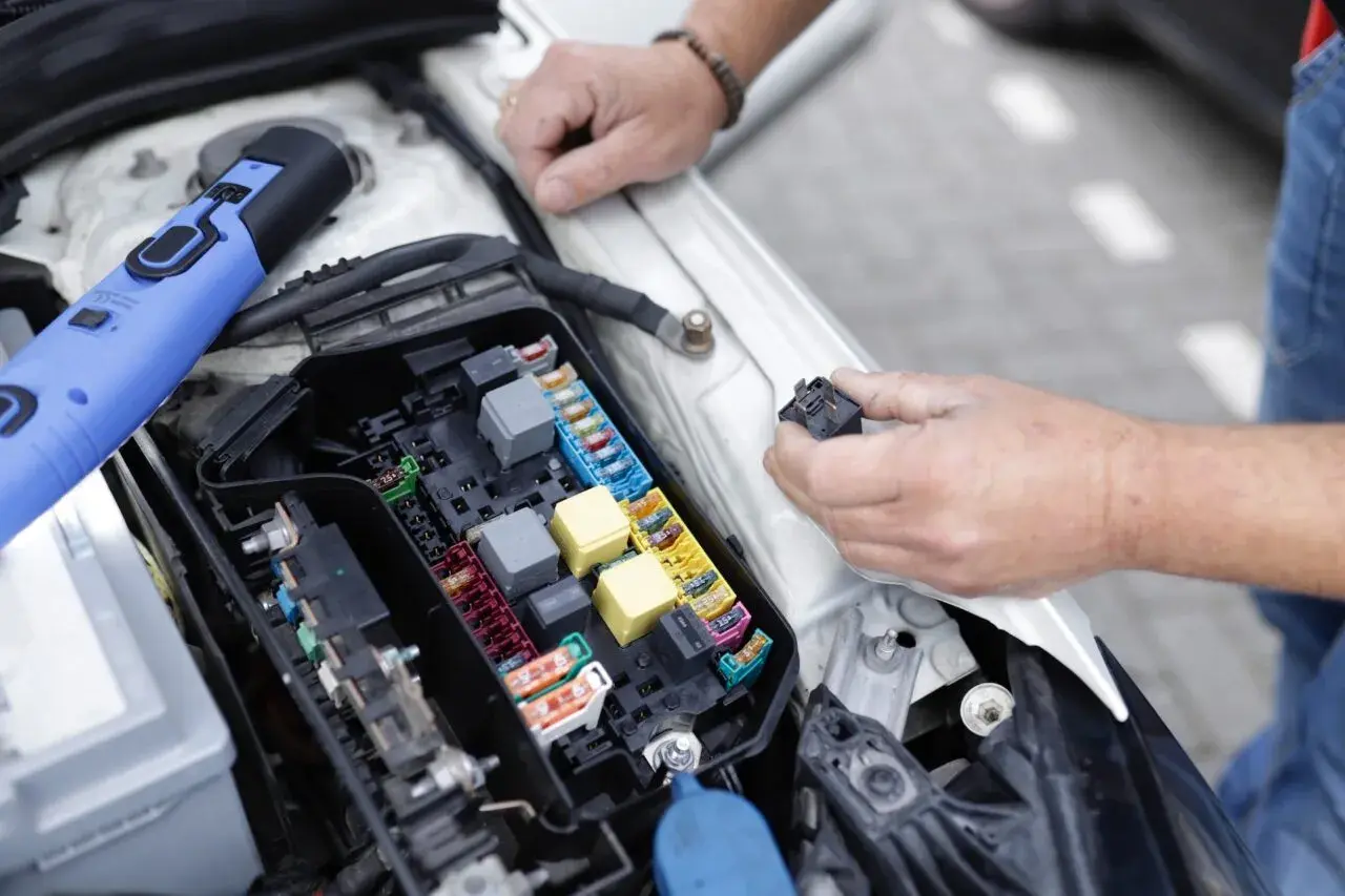 Un mécanicien examine le boîtier de fusibles d'une voiture, cherchant la cause d'un problème électrique. Il tient un relais dans sa main.