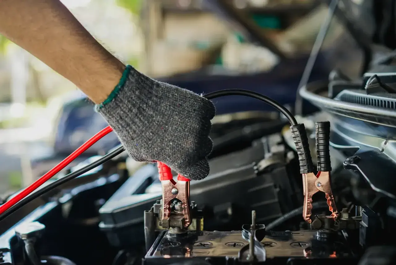 Main tenant un câble pour démarrer une voiture. La pince rouge est connectée à la batterie.