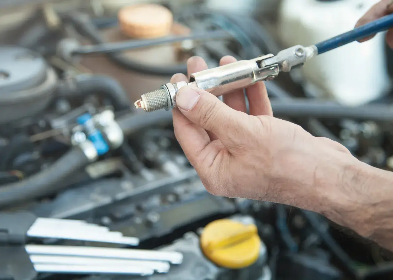 Main d'un mécanicien tenant une bougie d'allumage, prête à être installée dans le moteur d'une voiture.