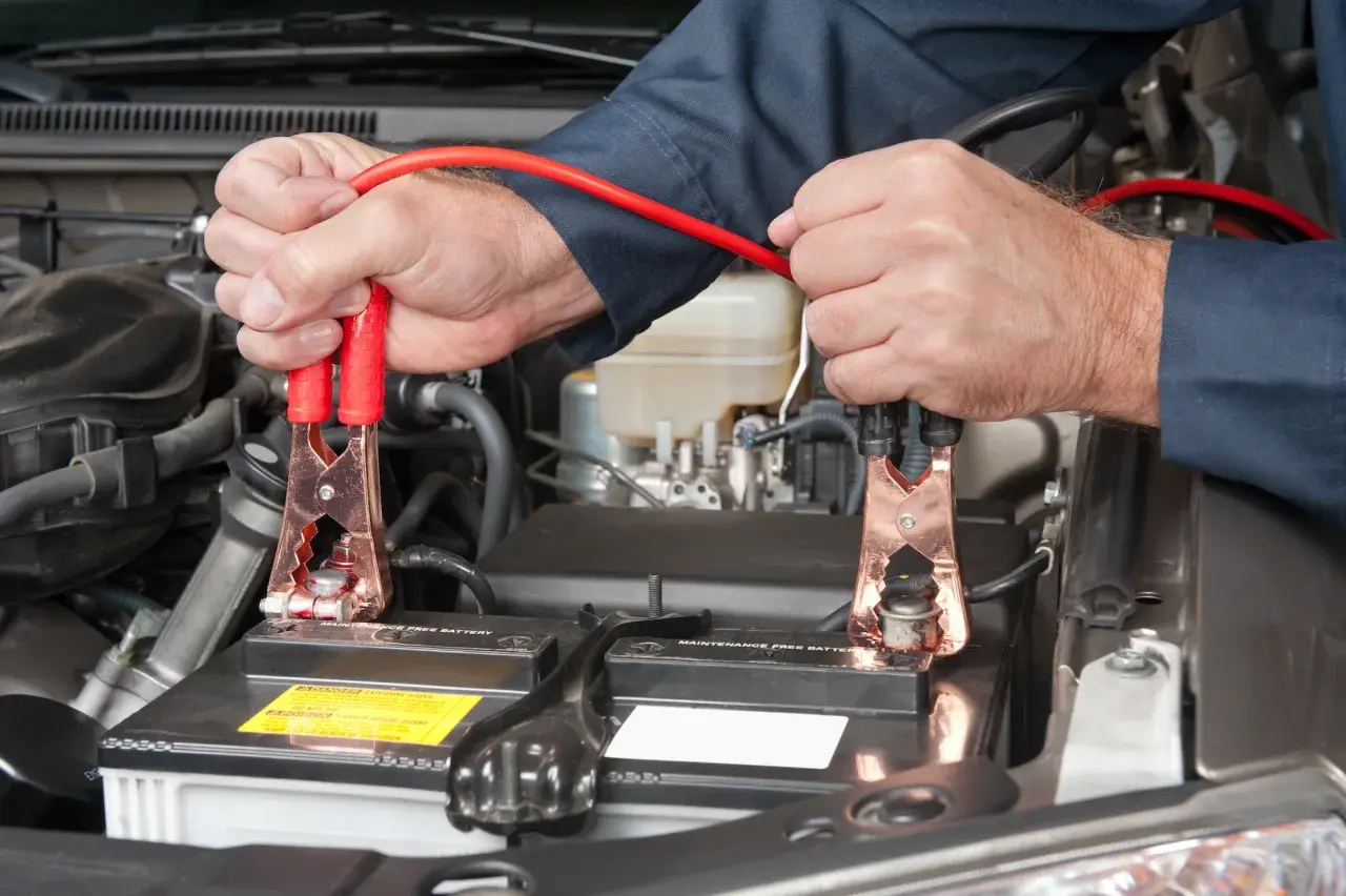Mains de mécanicien connectant des câbles de démarrage à une batterie de voiture. On peut charger une batterie sans la débrancher.