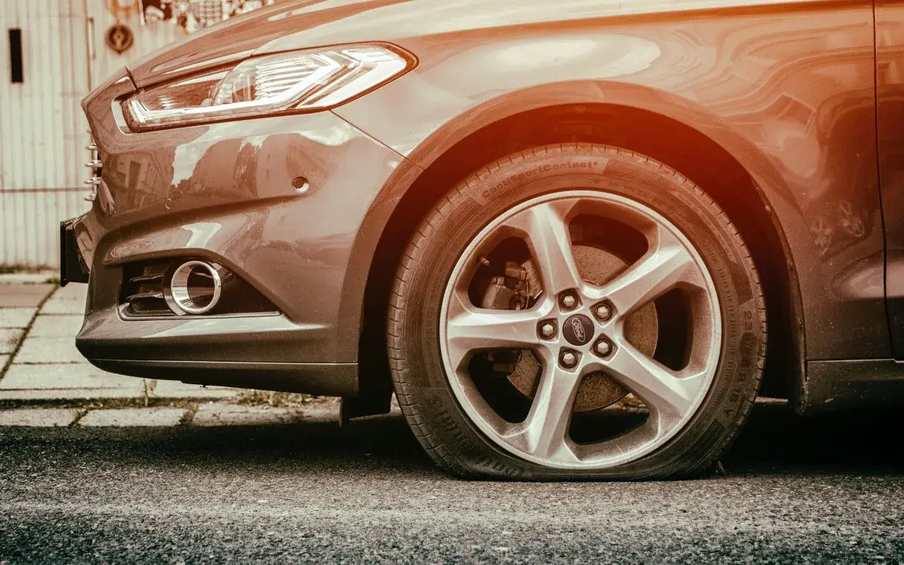 Gros plan sur une roue de voiture Ford avec un pneu crevé, le flanc complètement à plat sur l'asphalte. Une vraie galère !