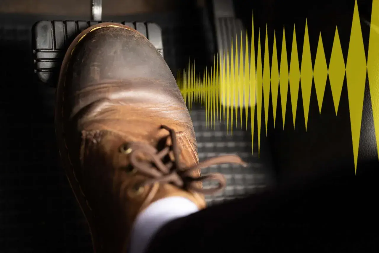 Un pied en chaussure marron appuie sur la pédale de frein, symbolisant le bruit frottement freinage.