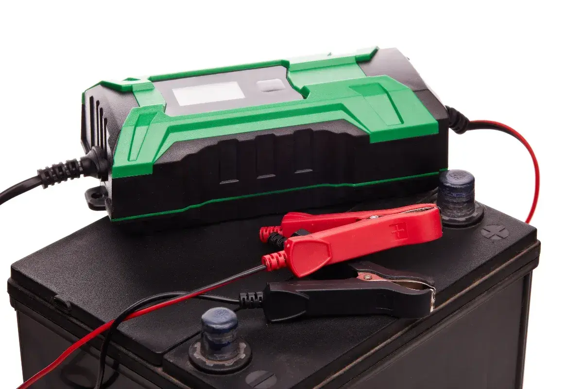 Chargeur de batterie vert et noir connecté à une batterie de voiture. Idéal pour le maintien de charge batterie sans débrancher.