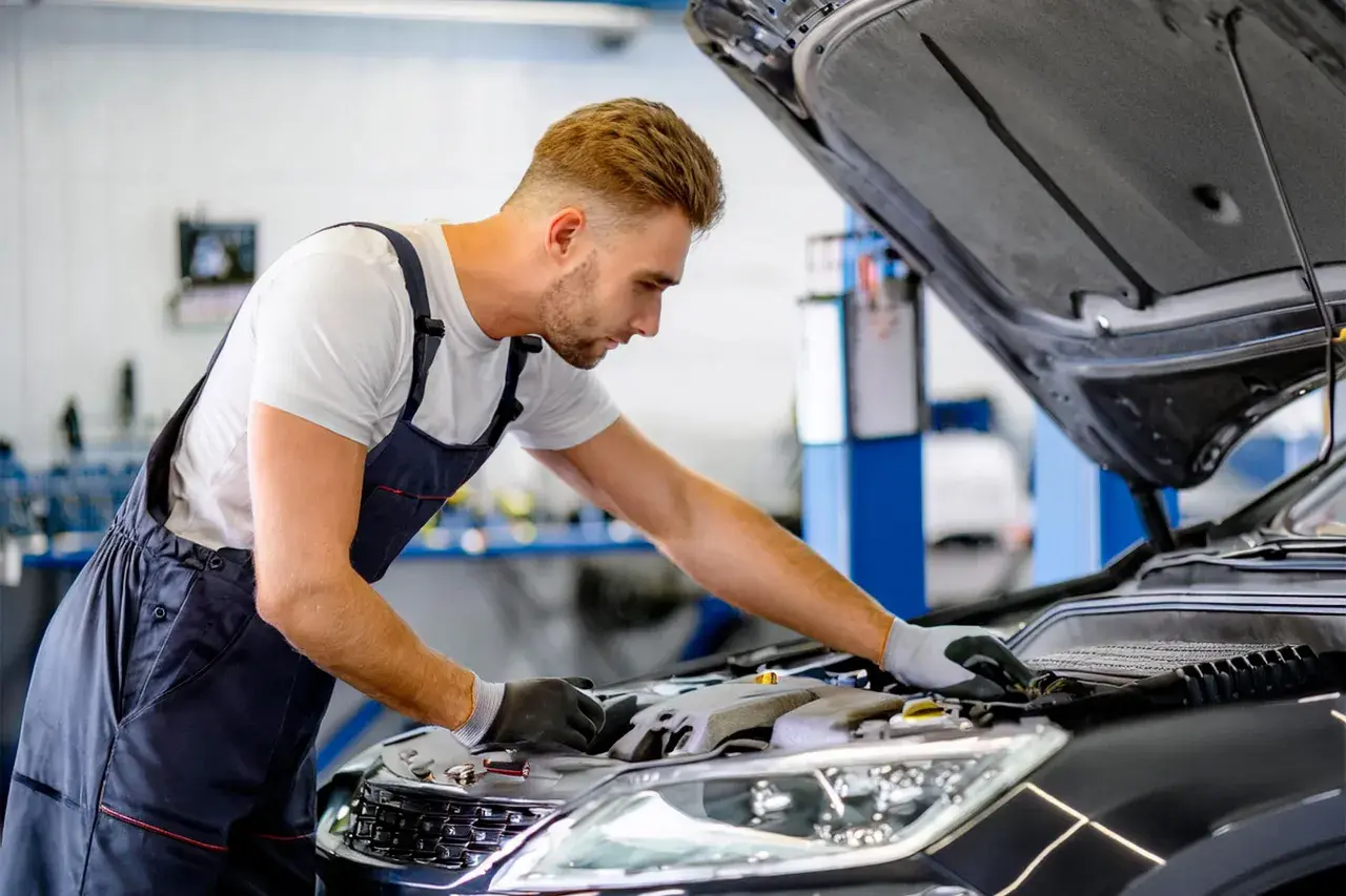 Mécanicien concentré sur le moteur d'une voiture, cherchant une astuce pour essuie glace en panne.