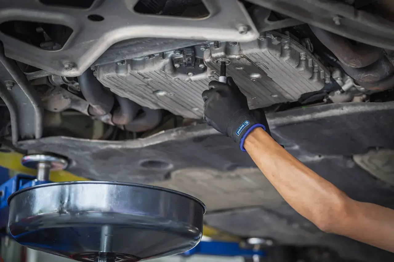 Main d'un mécanicien en gant noir dévissant le bouchon de vidange d'une voiture diesel. Le prix de la vidange voiture diesel est une préoccupation pour de nombreux propriétaires.