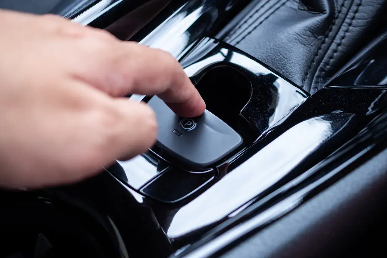 Main d'une personne appuyant sur le bouton du frein à main automatique. Voici comment débloquer un frein à main automatique.