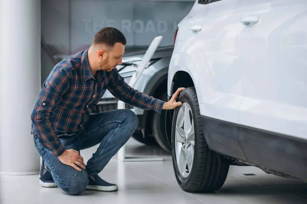 Un homme vérifie un pneu de voiture, peut-être parce que mes pneus font du bruit quand je roule.