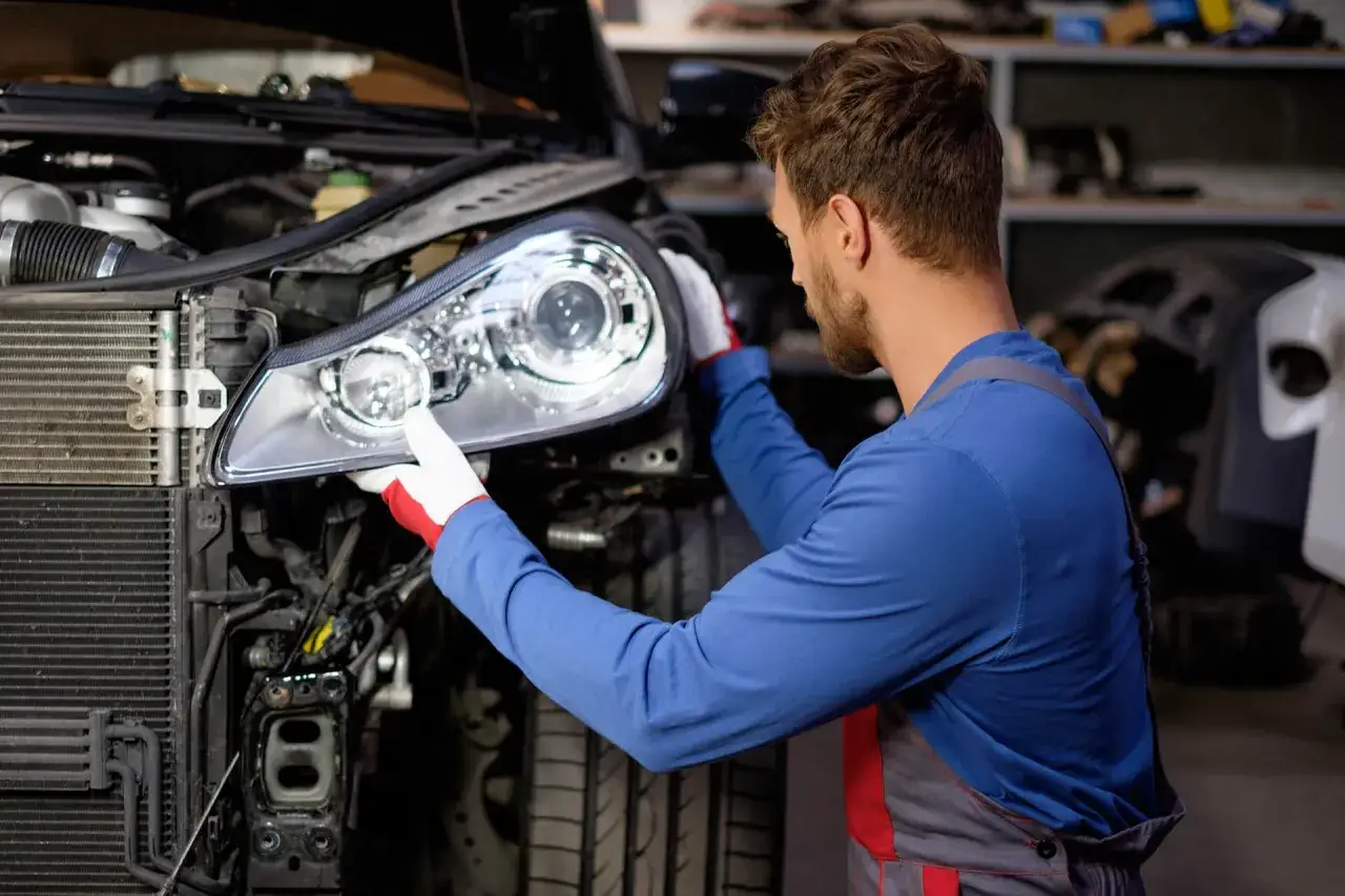 Mécanicien ajustant un phare de voiture, peut-être pour corriger une baisse d'intensité.