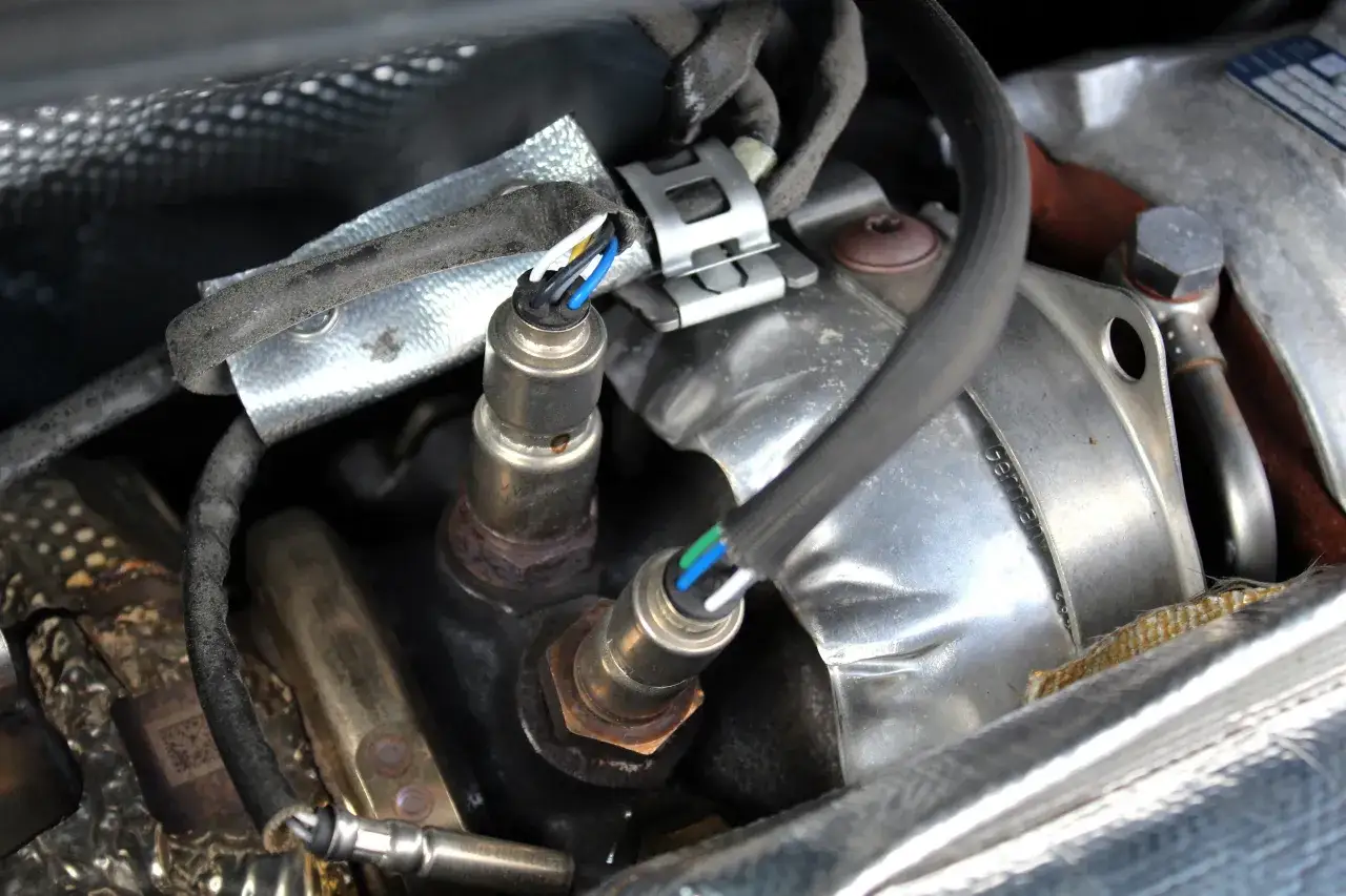 Deux sondes lambda rouillées, un symptôme de sonde lambda défectueuse, sont visibles sous un blindage thermique.