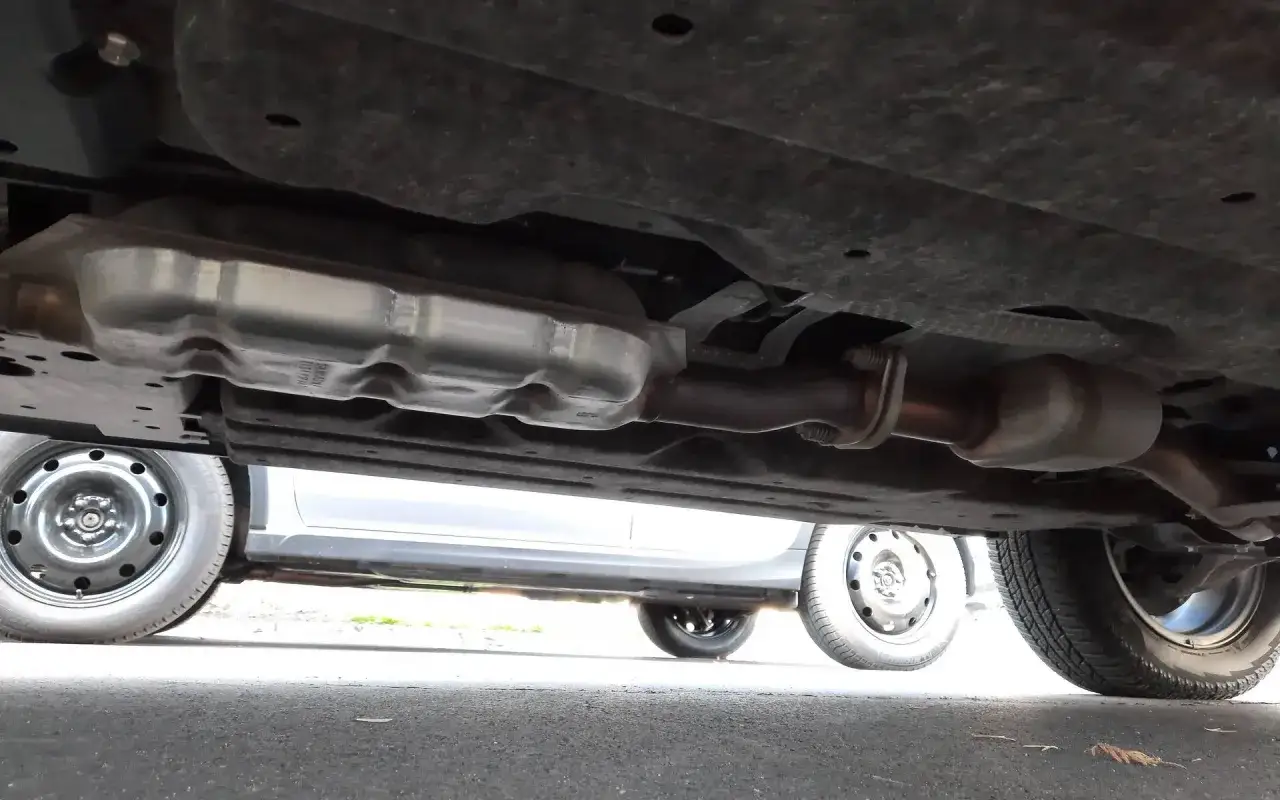Vue sous une voiture montrant le système d'échappement, y compris le catalyseur. Un symptôme catalyseur HS essence peut causer des problèmes de performance.