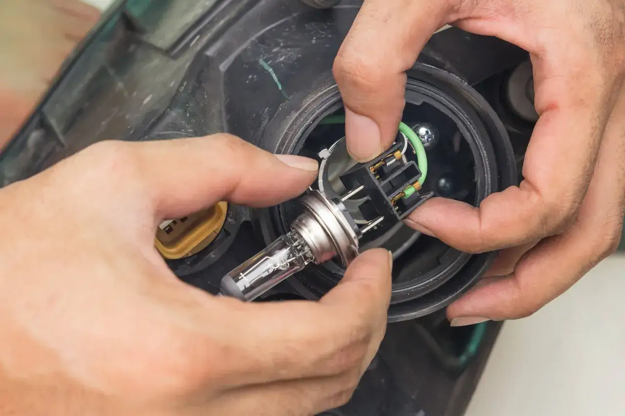 Mains pour changer les ampoules d'un phare de voiture. L'ampoule neuve est tenue près de son logement.