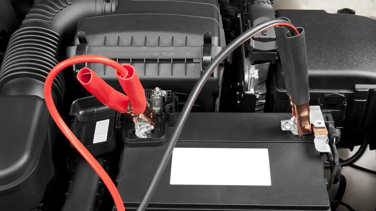 Pinces de démarrage rouges connectées à une batterie de voiture. Aide à choisir quel booster de batterie choisir.