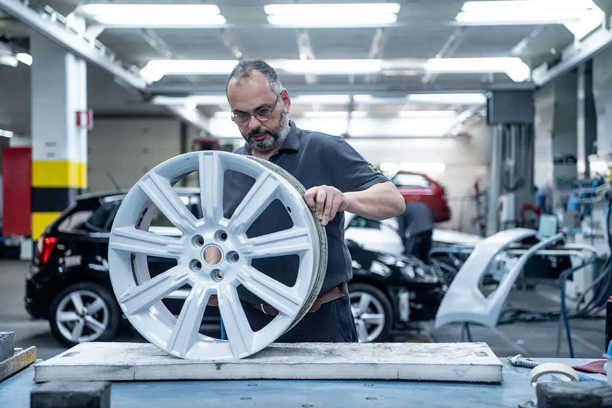 Un homme examine une jante alu dans un atelier. Il est prêt à la réparer pour lui redonner son éclat.
