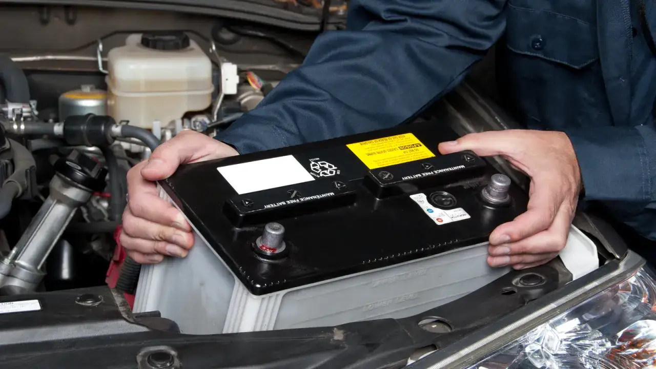 Mains de mécanicien retirant une batterie de voiture. Il faut débrancher batterie avant de la manipuler.