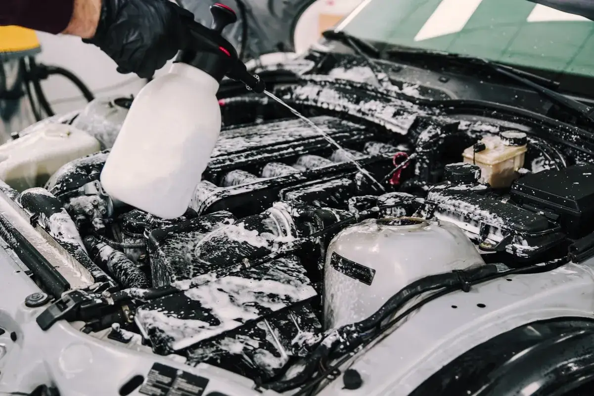 Main moteur de voiture couvert de mousse. Une main gantée utilise un pulvérisateur pour aider à comment décrasser une voiture.