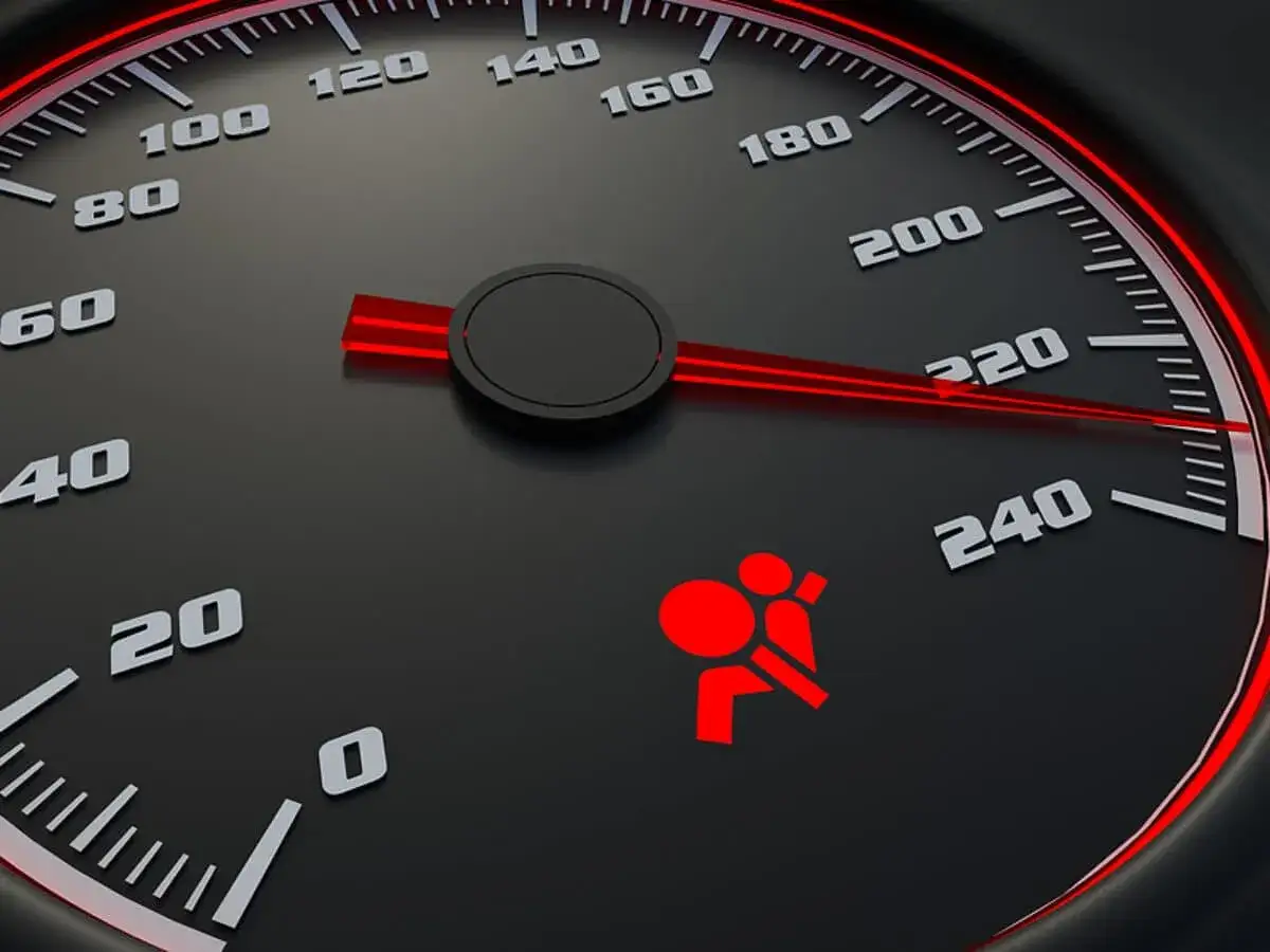 Tableau de bord d'une voiture avec un voyant rouge allumé indiquant un problème airbag. Le compteur de vitesse est visible.