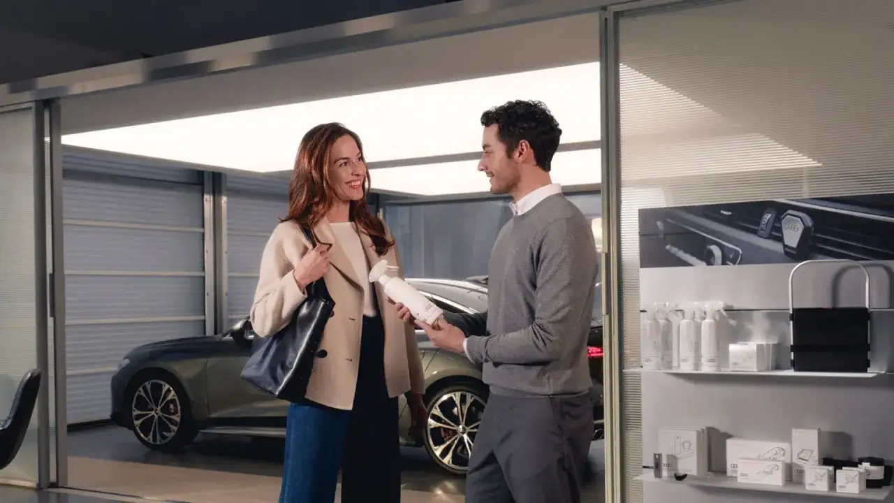 Un homme présente un produit d'entretien à une femme devant une Audi. Le tarif entretien Audi Q3 est discuté.