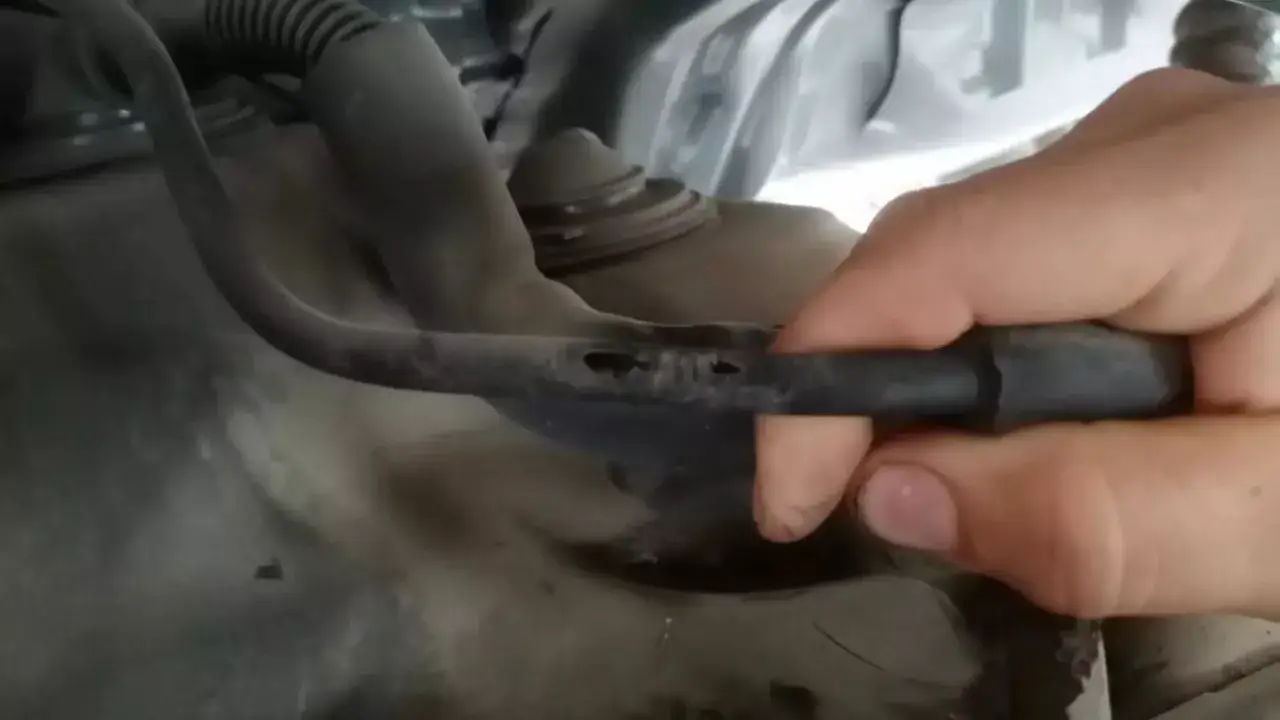 Main d'une personne inspectant un flexible de frein endommag&eacute; avec plusieurs perforations visibles.