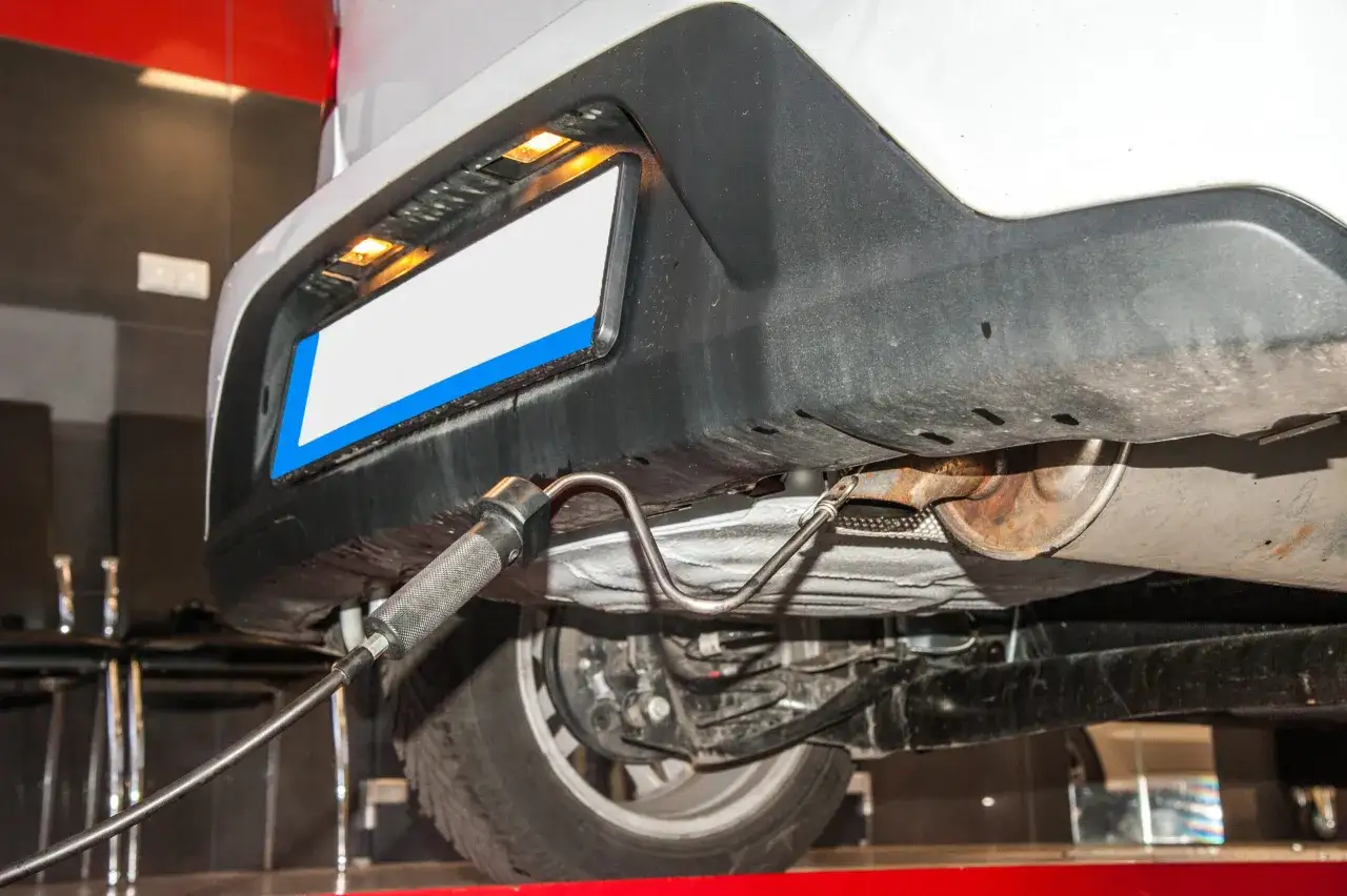 Sonde insérée dans l'échappement d'une voiture pour un contrôle des émissions. Le système semble ancien, rendant le contrôle impossible des émissions à l'échappement.