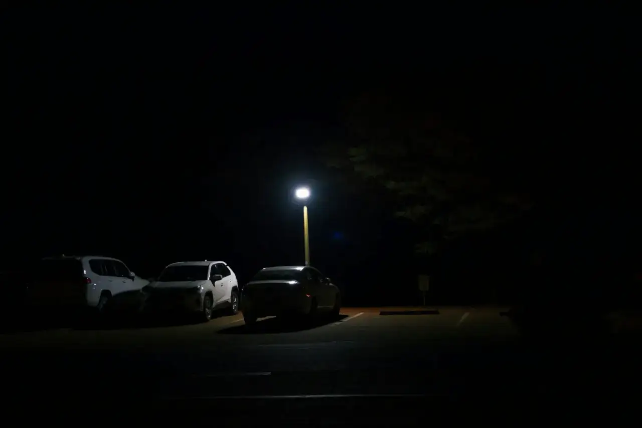 Trois voitures garées la nuit sous un lampadaire. Les feux de position des véhicules sont faiblement allumés, créant une atmosphère paisible.