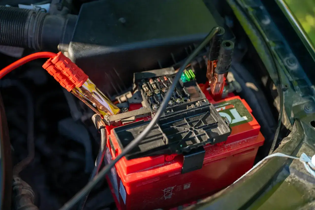 Une batterie de voiture rouge est connectée à un chargeur avec des pinces rouges et noires. La batterie qui ne charge pas avec chargeur est au centre de l'image.