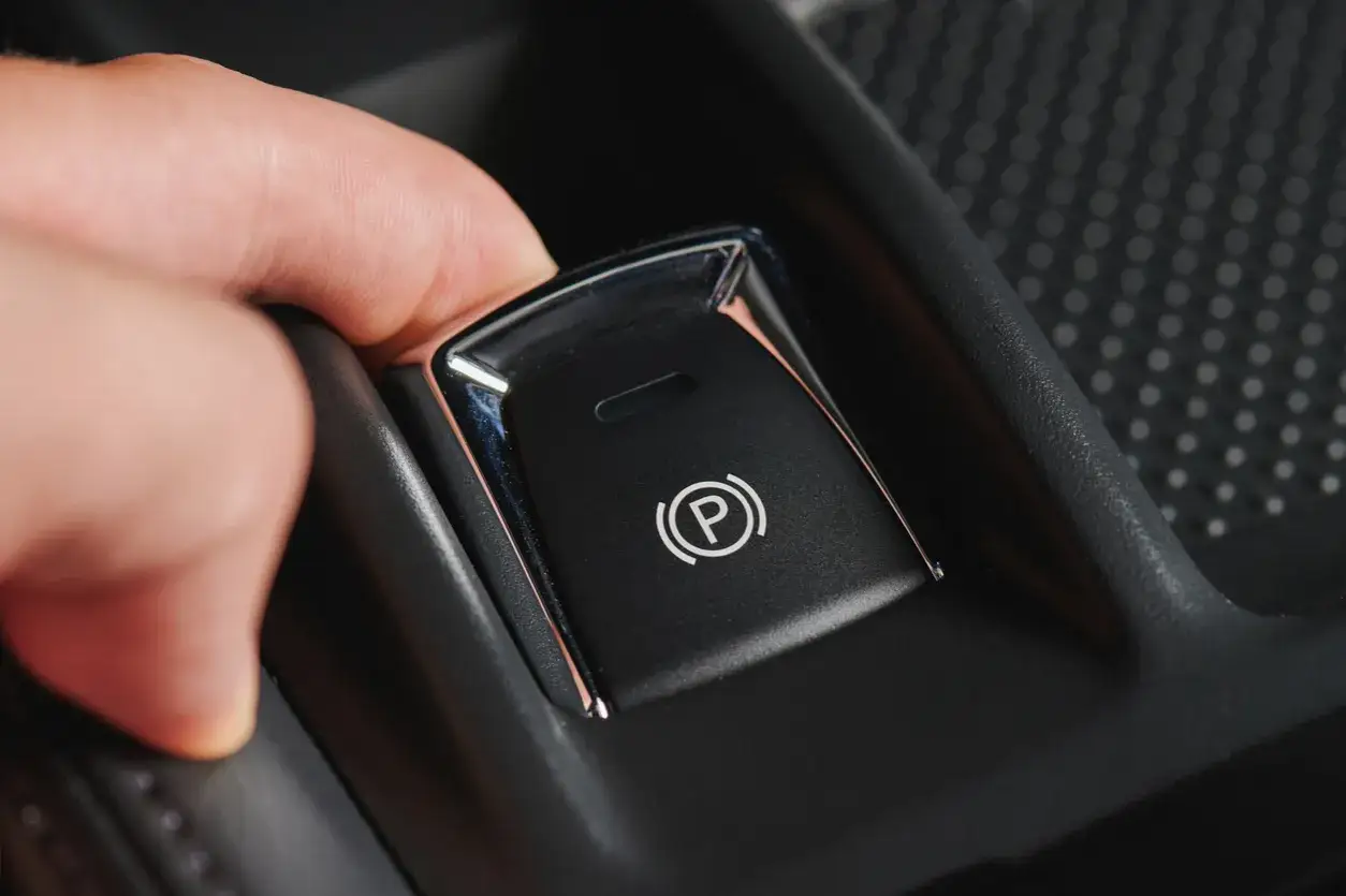 Main d'une personne appuyant sur le bouton du frein &agrave; main automatique pour le d&eacute;bloquer.