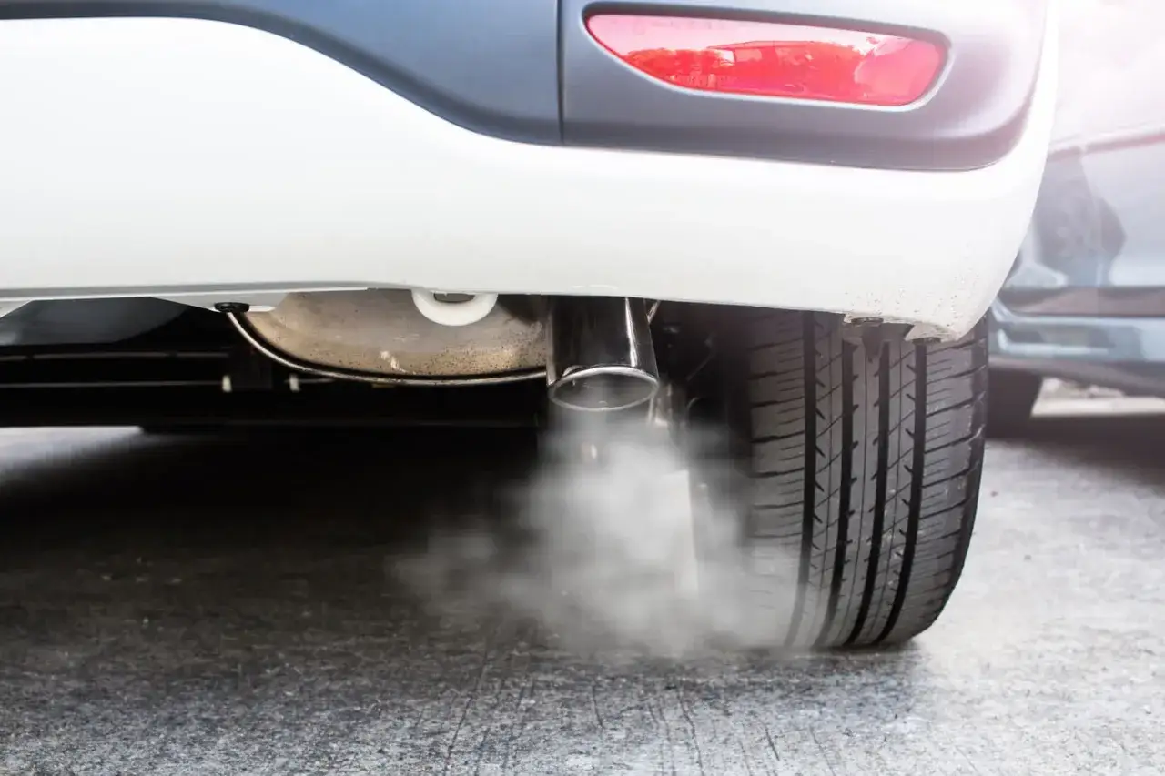 Fumée blanche s'échappe du pot d'échappement d'une voiture, signe d'une combustion en cours.