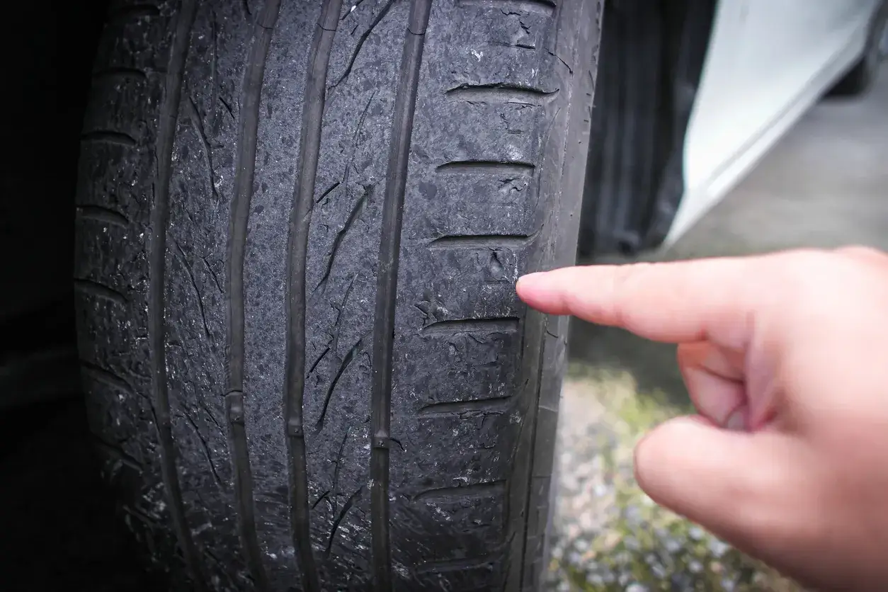 Doigt pointant un pneu us&eacute;, signe d'un possible probl&egrave;me de prix d'une g&eacute;om&eacute;trie voiture.